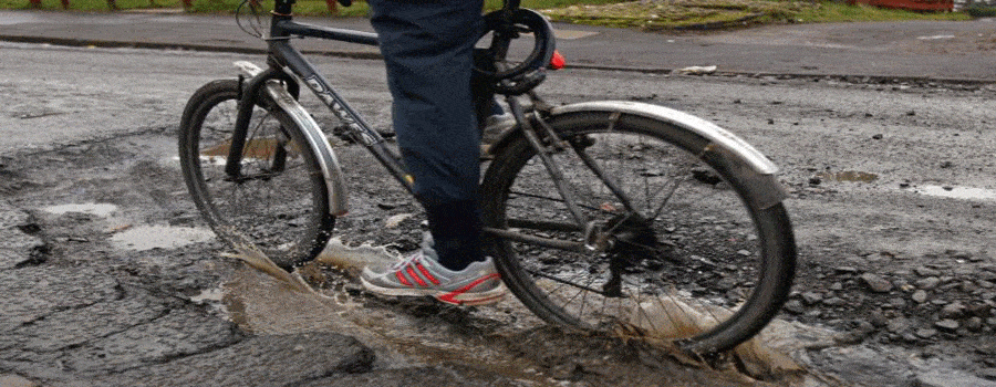 a cyclist pedalling through a puddle on a damaged road